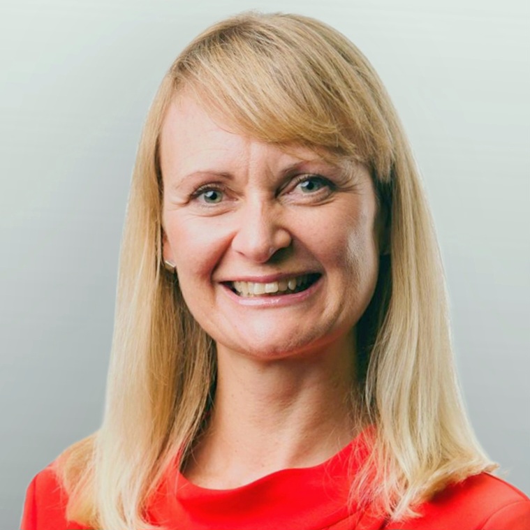 Natalie is wearing a bright red top and has long blonde hair, smiles widely at the camera
