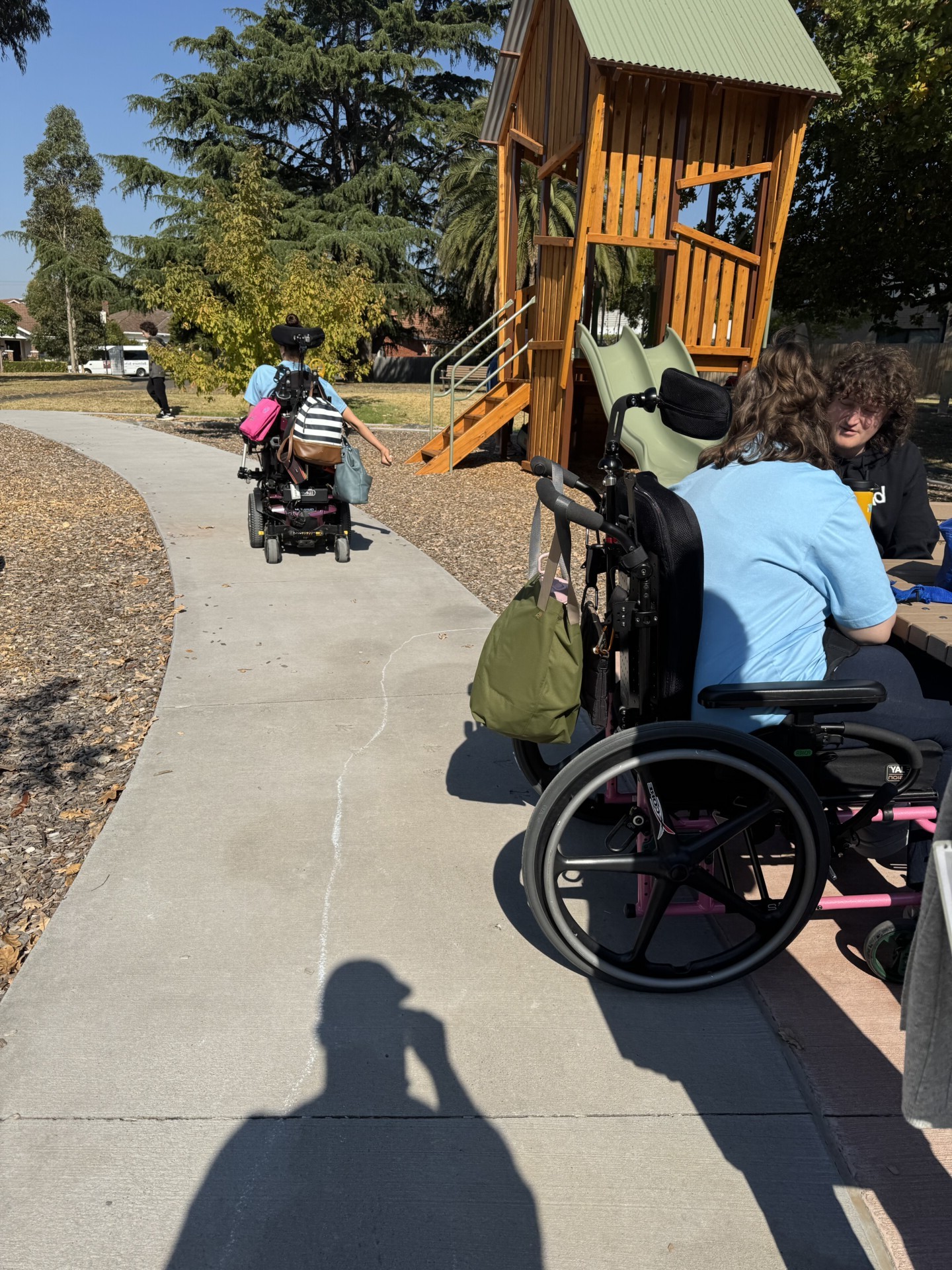 Wheelchair users are moving around a playground space in the sunshine