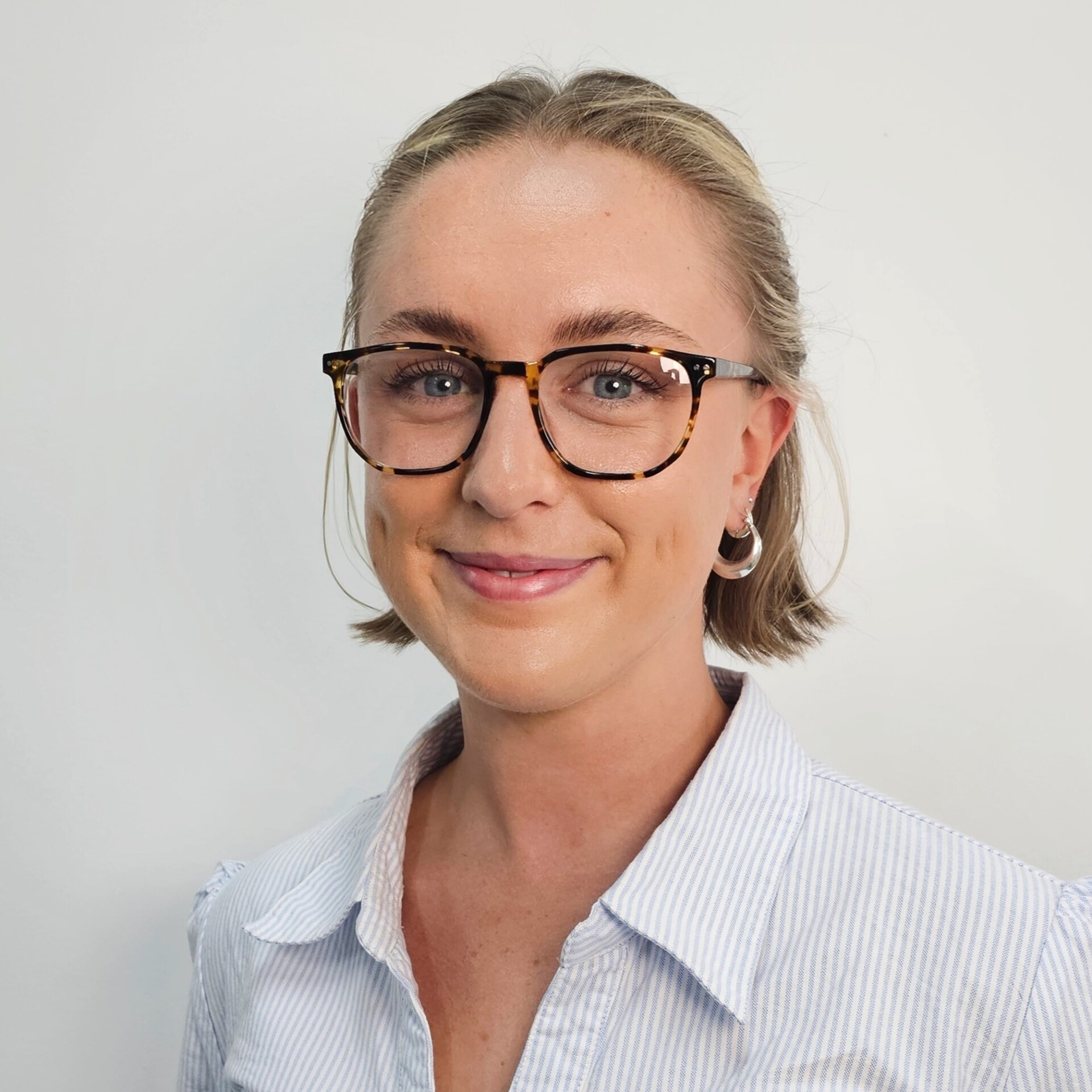 A smiling Caity wears dark glasses and a light collared shirt. Her hair is short and light.