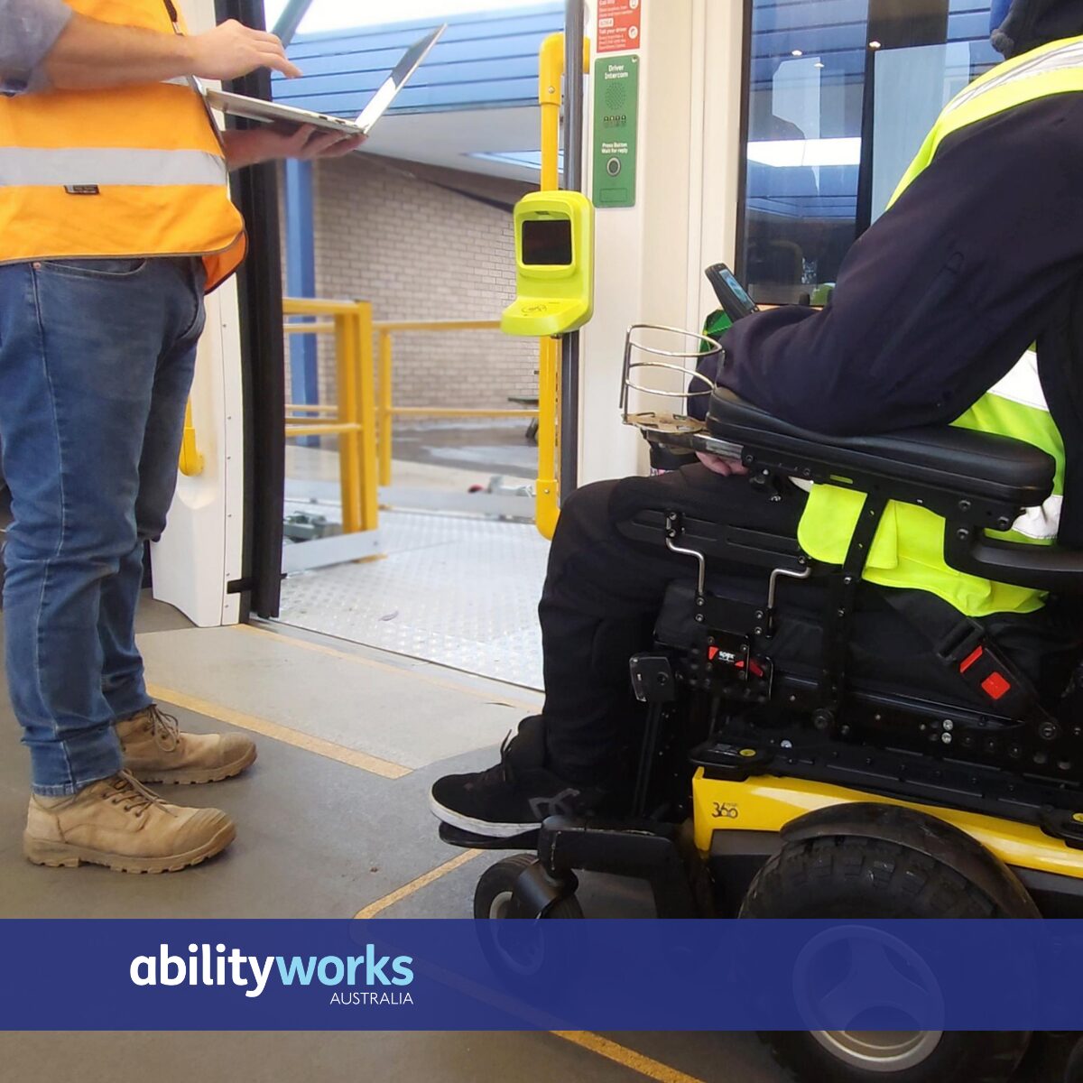 A wheelchair user and a colleague in high-visibility vests review transport accessibility features using a laptop and ticket machine on a tram.